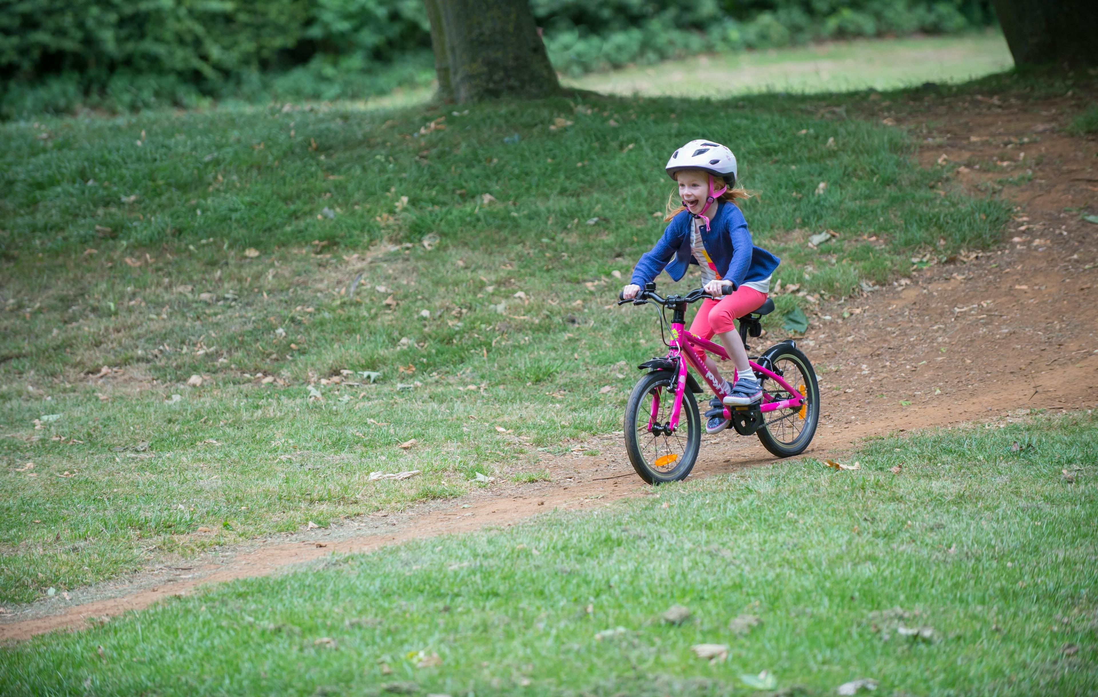 Young girl cycling through a field on a pink bicycle